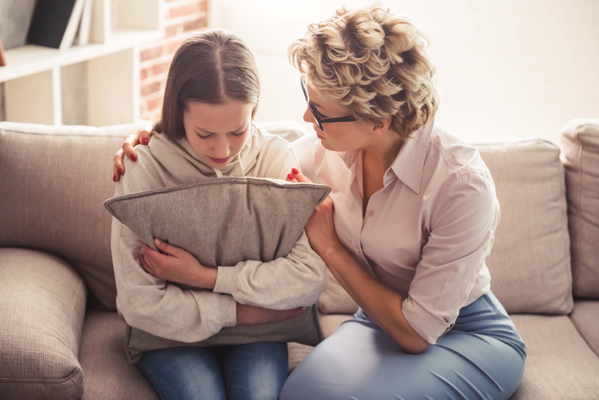 A woman is sitting on a couch with a young girl holding a pillow.