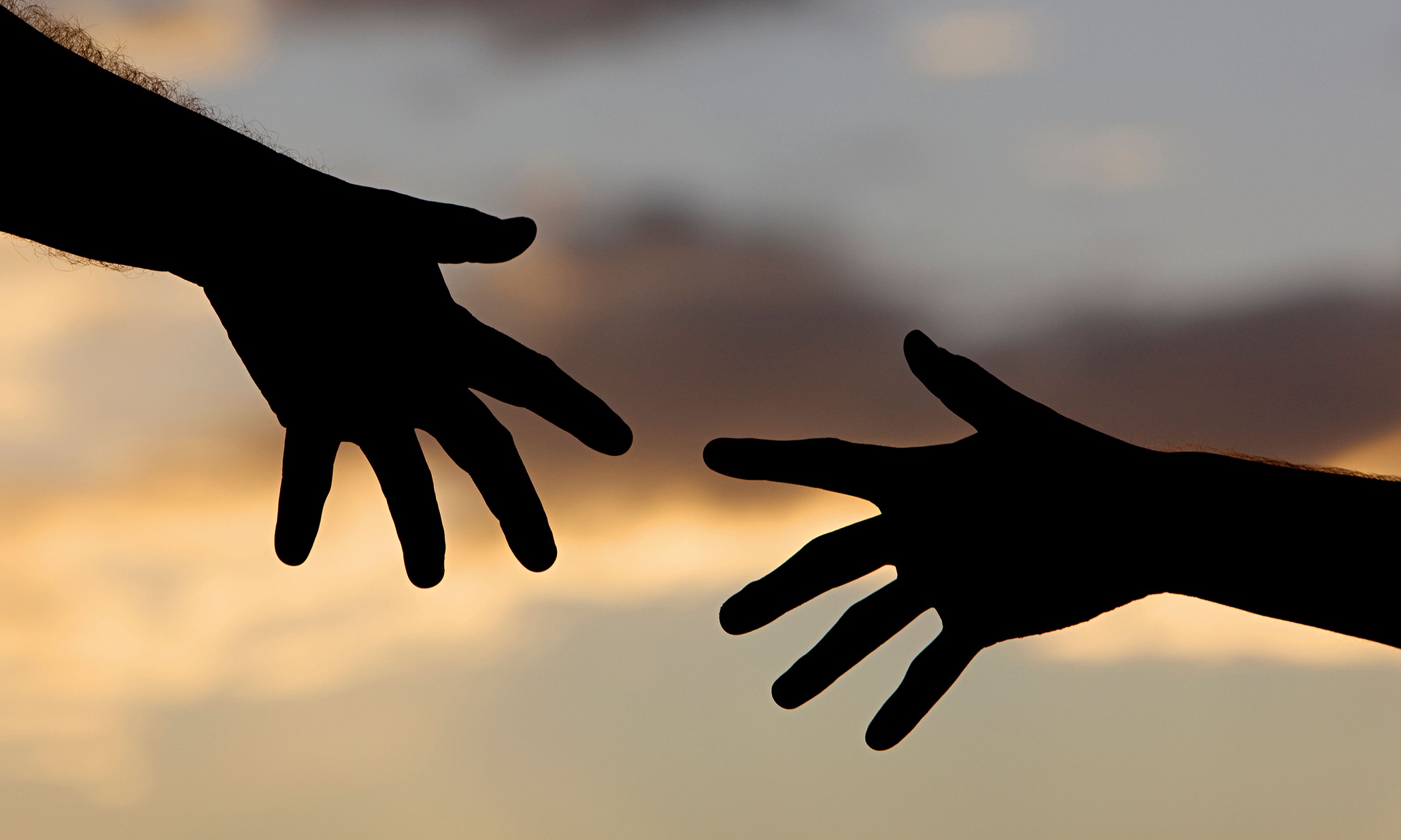 Silhouette of two hands reaching for each other at sunset.